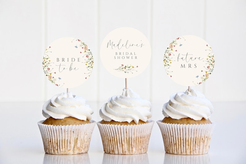 May include: Three cupcakes with white frosting topped with round paper circles. The circles have floral designs and text that reads "Bride to be", "Madeline's Bridal Shower", and "Future Mrs."