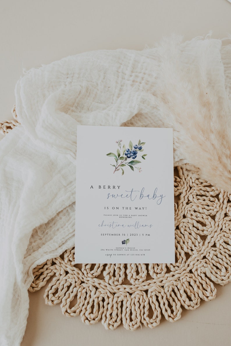 Może przedstawiać: Zaproszenie na baby shower z akwarelową ilustracją jag&oacute;d i zieleni. Zaproszenie zawiera napis "A Berry Sweet Baby Is On The Way!" oraz datę i godzinę baby shower, imię osoby, kt&oacute;rej dotyczy uroczystość, oraz miejsce.
