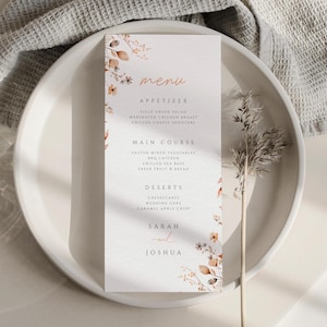 May include: A wedding menu card with floral accents, featuring the word "menu" in a handwritten style. The menu lists appetizers, main courses, and desserts, with the names "Sarah" and "Joshua" at the bottom.