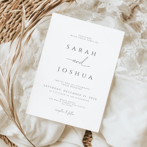 K&ouml;nnte beinhalten: Eine wei&szlig;e Hochzeitseinladung mit schwarzem Text, mit den Namen "Sarah und Joshua" in eleganter Schrift. Die Einladung enth&auml;lt Datum, Uhrzeit und Ort der Hochzeit. Die Einladung liegt auf einem wei&szlig;en Spitzentuch und einem geflochtenen Korb.