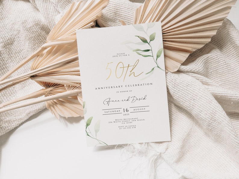 Pu&ograve; includere: Un invito bianco con lettere dorate che annunciano una celebrazione del 50&deg; anniversario per Anne e David. La carta presenta un'illustrazione ad acquerello di foglie verdi e fiori bianchi.