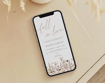 May include: A smartphone displays a bridal shower invitation with the words "Fall in Love" in elegant script. The invitation includes details for Rachel Garcia's shower on October 18, 2026, at The White Restaurant. Floral accents in neutral tones adorn the bottom.