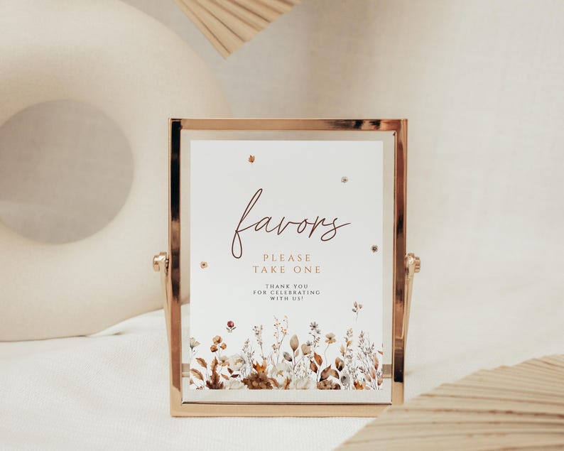 May include: A gold-framed sign with the word "favors" in elegant script. The sign reads "Please take one" and "Thank you for celebrating with us!" Floral illustrations in muted tones adorn the bottom edge, creating a rustic aesthetic.