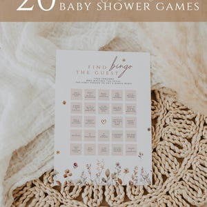 May include: A baby shower game card with the text "20 Editable Baby Shower Games" at the top. The card features a "Find the Guest Bingo" game with floral accents and a neutral color palette. The card is on a woven mat.