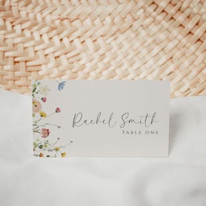 May include: A white table card with a floral design on the left side and the text "Rachel Smith Table One" on the right side.