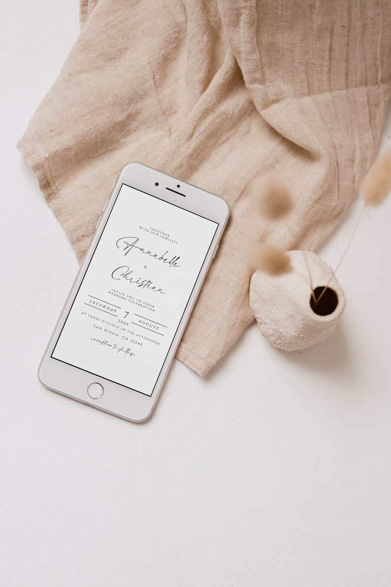 May include: A white smartphone displaying a wedding invitation for Annabelle and Christian. The invitation is for a wedding ceremony on Saturday, August 7, 2024, at three o'clock in the afternoon in San Diego, CA 12345.
