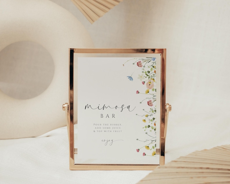 May include: A gold-framed sign with a floral border and the text "mimosa bar" in cursive. The sign also includes instructions for making a mimosa: "Pour the bubbly, add some juice & top with fruit, enjoy."