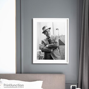 Pu&ograve; includere: Fotografia in bianco e nero di un uomo in abito e cappello. &Egrave; in piedi con le braccia incrociate e guarda di lato. La foto &egrave; incorniciata in una cornice bianca.