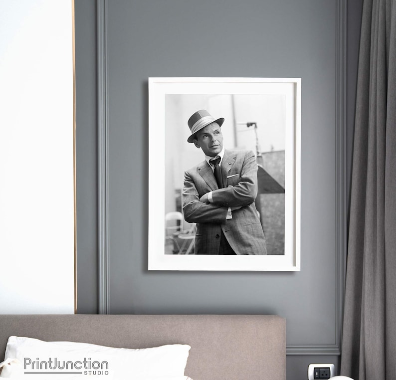 Pu&ograve; includere: Fotografia in bianco e nero di un uomo in abito e cappello. &Egrave; in piedi con le braccia incrociate e guarda di lato. La foto &egrave; incorniciata in una cornice bianca.
