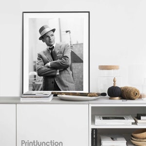 Pu&ograve; includere: Fotografia in bianco e nero di un uomo in abito e cappello. L'uomo &egrave; in piedi con le braccia incrociate. La foto &egrave; incorniciata da una cornice nera e appesa a un muro bianco sopra uno scaffale bianco.