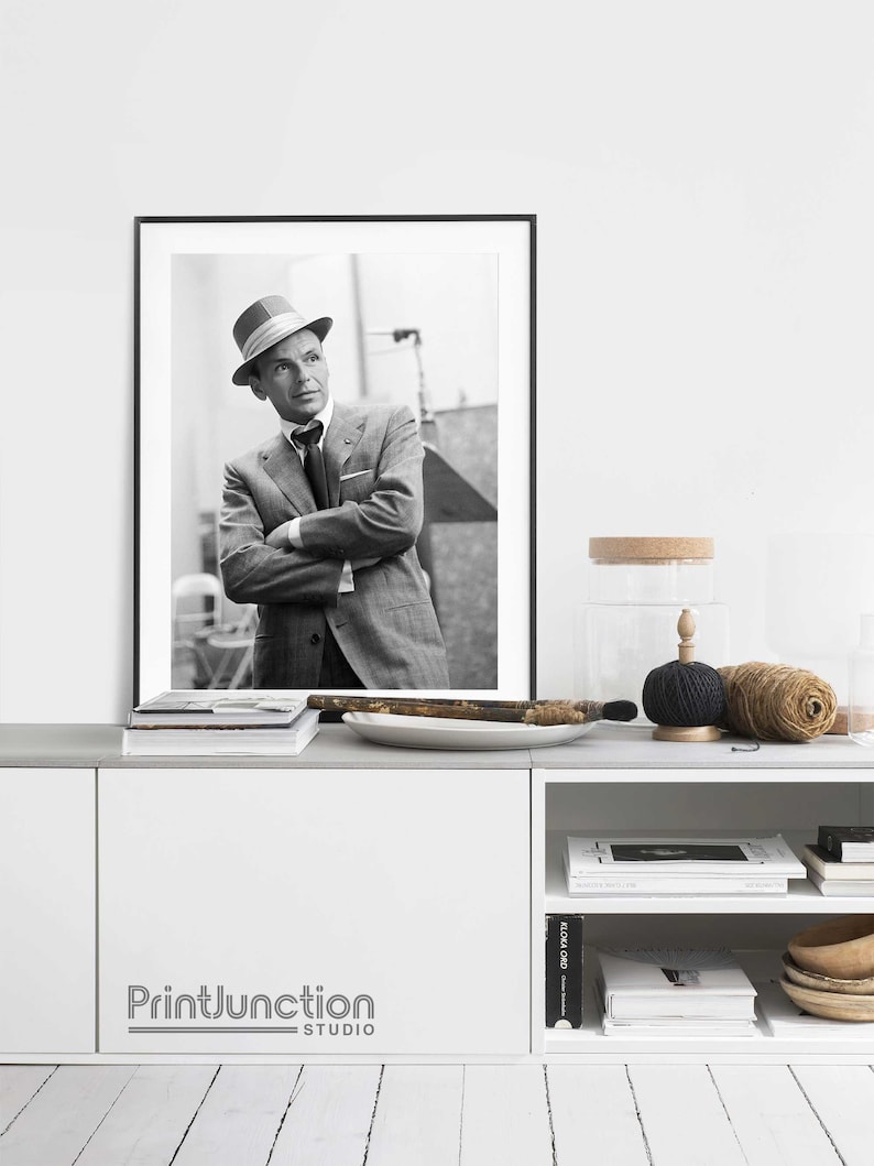 Pu&ograve; includere: Fotografia in bianco e nero di un uomo in abito e cappello. L'uomo &egrave; in piedi con le braccia incrociate. La foto &egrave; incorniciata da una cornice nera e appesa a un muro bianco sopra uno scaffale bianco.