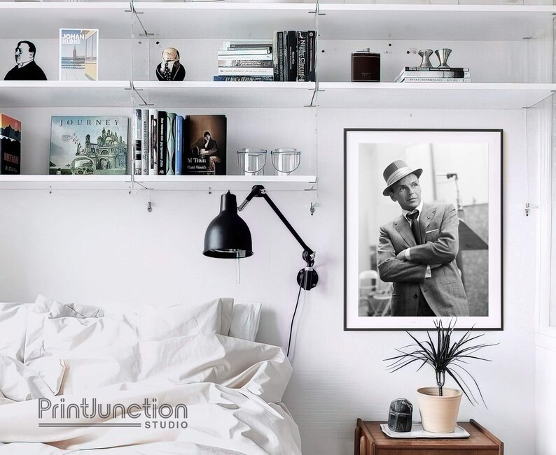 Pu&ograve; includere: Fotografia in bianco e nero di un uomo con un cappello fedora e un abito. L'uomo guarda di lato e ha un'espressione seria sul viso. La fotografia &egrave; incorniciata in una cornice nera e appesa a un muro bianco.