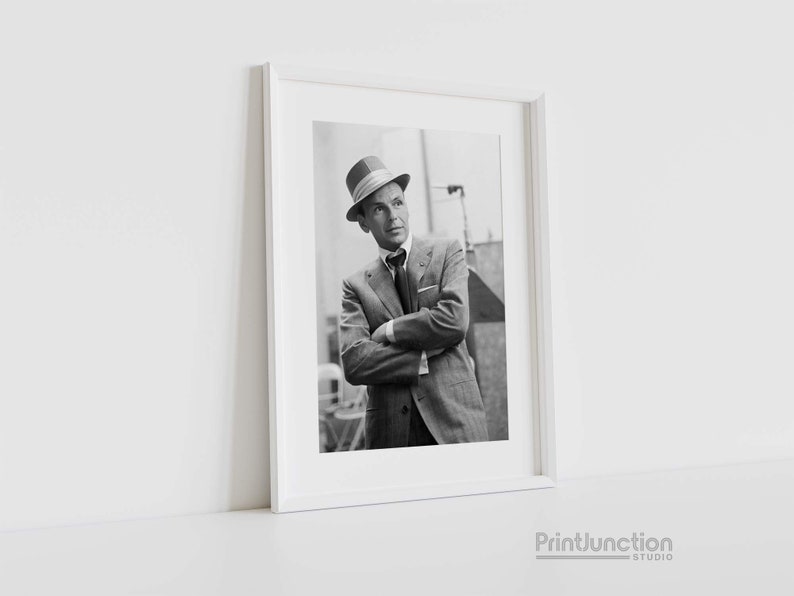 Pu&ograve; includere: Fotografia in bianco e nero di un uomo in abito e cappello. &Egrave; in piedi con le braccia incrociate e guarda in alto.