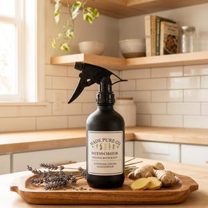 May include: A black spray bottle labeled "Made Pure Co. Midsomer Natural Room Scent" with lavender, ginger, and sandalwood. The bottle sits on a wooden tray with lavender sprigs and ginger root. The background includes wooden shelves and a window.