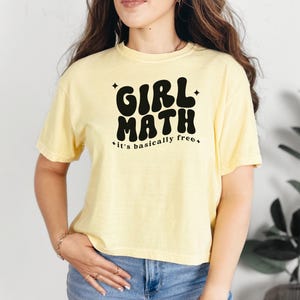 Puede incluir: Una camiseta de manga corta de color amarillo p&aacute;lido con el texto en negro GIRL MATH y it's basically free, decorada con peque&ntilde;as estrellas de cuatro puntas. La prenda tiene cuello redondo y un corte holgado en tejido de algod&oacute;n.