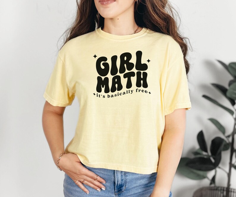Puede incluir: Una camiseta de manga corta de color amarillo p&aacute;lido con el texto en negro GIRL MATH y it's basically free, decorada con peque&ntilde;as estrellas de cuatro puntas. La prenda tiene cuello redondo y un corte holgado en tejido de algod&oacute;n.