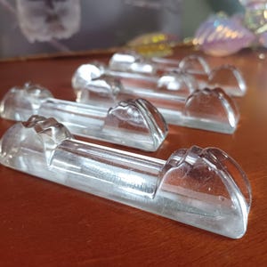 Op de afbeelding: Een set van vier eetstokjessteunen van helder glas, elk met een lange, rechthoekige basis met twee verhoogde, afgeronde uiteinden die een subtiel, getrapt ontwerp hebben. De transparante glazen stukken zijn in een verspringend patroon geplaatst.