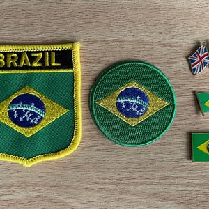 以下が含まれることがあります： ブラジルをテーマにしたアイテムのコレクション。刺繍パッチ2つ、丸いパッチ1つ、旗ピン3つが含まれています。パッチとピンは、ブラジル国旗の緑、黄色、青、白の色を使用しています。パッチには黒字で「BRAZIL」と書かれています。