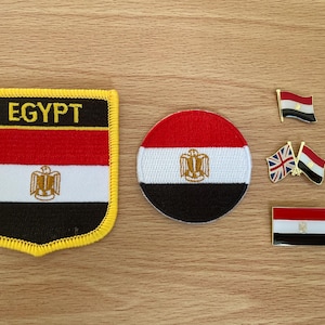Op de afbeelding: Een verzameling items met het thema Egyptische vlag. Inclusief een patch met de tekst "EGYPT", een ronde patch en drie pins. De items tonen de rode, witte en zwarte kleuren van de Egyptische vlag, met een gouden embleem.
