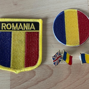 May include: A collection of Romanian flag-themed items. Includes a shield-shaped patch with "ROMANIA" and a circular patch, both featuring blue, yellow, and red vertical stripes. Also, two flag pins, one with the UK flag and Romanian flag, and a single Romanian flag pin.