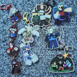 Puede incluir: Una colección de llaveros de acrílico con varias ilustraciones de personajes estilizados y de formas bloqueadas con colores vibrantes, diversos atuendos y accesorios, incluyendo una cadena vertical larga, dijes individuales y un diseño en forma de botella.