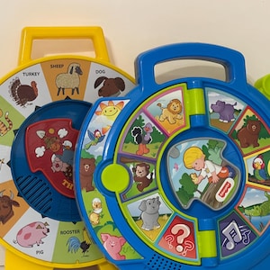 May include: Two colorful Fisher-Price toy learning wheels. One is yellow and the other is blue. Each wheel features illustrations of animals and a handle for carrying. The yellow wheel has animal names like "cat" and "dog". The blue wheel has a child figure.
