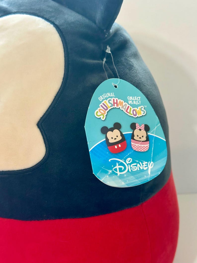 Op de afbeelding: Een groot, pluche Mickey Mouse Squishmallow-speelgoed. Het speelgoed is voornamelijk zwart, rood en wit, met een label met Mickey en Minnie Mouse-illustraties en het Disney-logo. Op het label staat "Original Squishmallows" en "Collect Us All!"