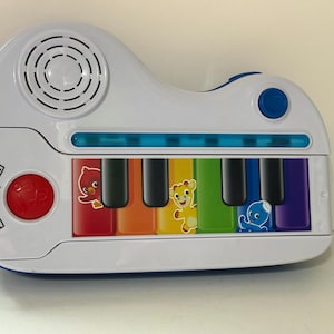 Pode incluir: Um piano de brinquedo Baby Einstein branco e azul com um alto-falante, um bot&atilde;o vermelho e um bot&atilde;o azul. As teclas do piano s&atilde;o coloridas com personagens de desenhos animados. O piano &eacute; projetado para crian&ccedil;as pequenas.