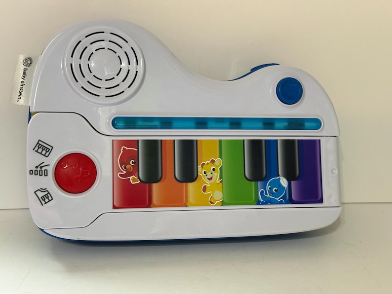 Pode incluir: Um piano de brinquedo Baby Einstein branco e azul com um alto-falante, um bot&atilde;o vermelho e um bot&atilde;o azul. As teclas do piano s&atilde;o coloridas com personagens de desenhos animados. O piano &eacute; projetado para crian&ccedil;as pequenas.