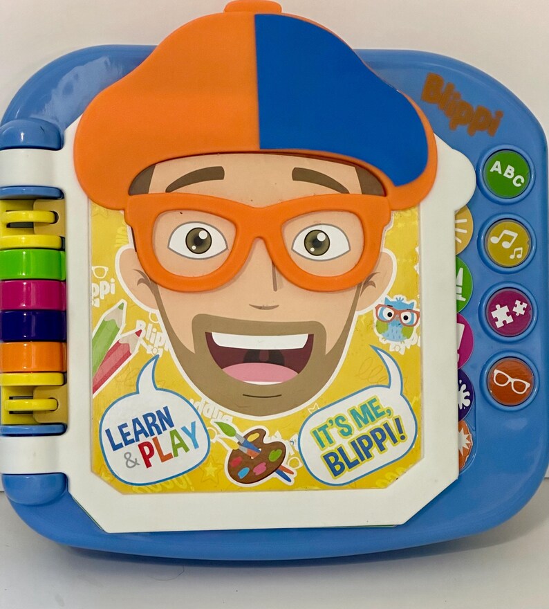 May include: A blue and white children's learning toy featuring a cartoon character with orange glasses and a hat. The toy has buttons with icons and the text "Learn & Play" and "It's Me, Blippi!"