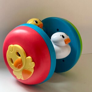 May include: A colorful toy featuring a rolling wheel design with a red and blue exterior. The toy has yellow and white duck figures. The toy is designed for children.