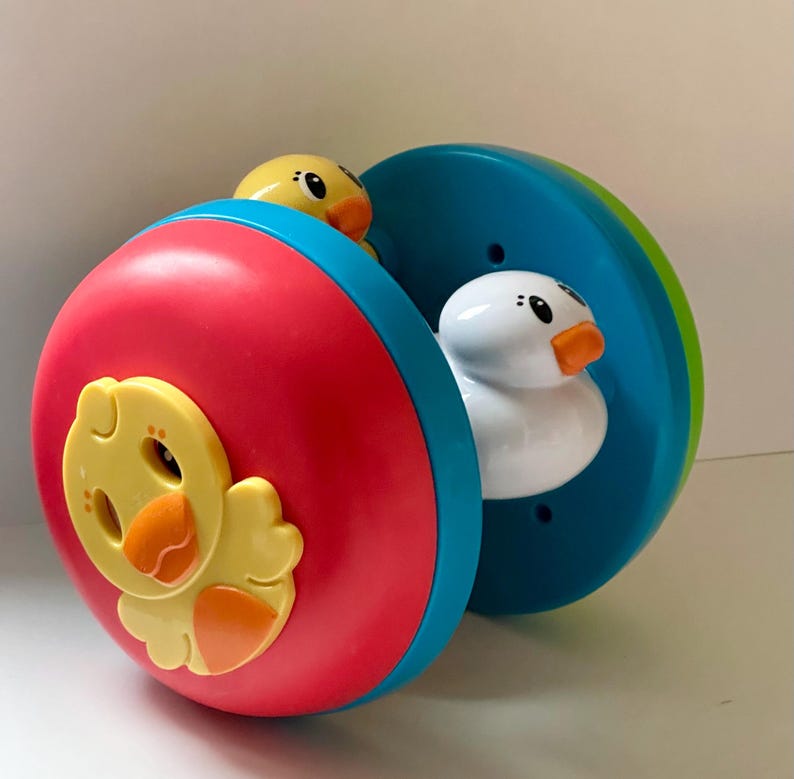 May include: A colorful toy featuring a rolling wheel design with a red and blue exterior. The toy has yellow and white duck figures. The toy is designed for children.