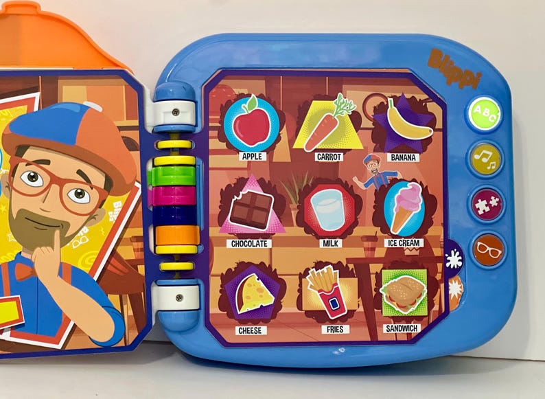 May include: A blue and orange Blippi learning toy with colorful buttons and illustrations of food items like an apple, carrot, and ice cream. The toy has a flip-open design and features a cartoon character.
