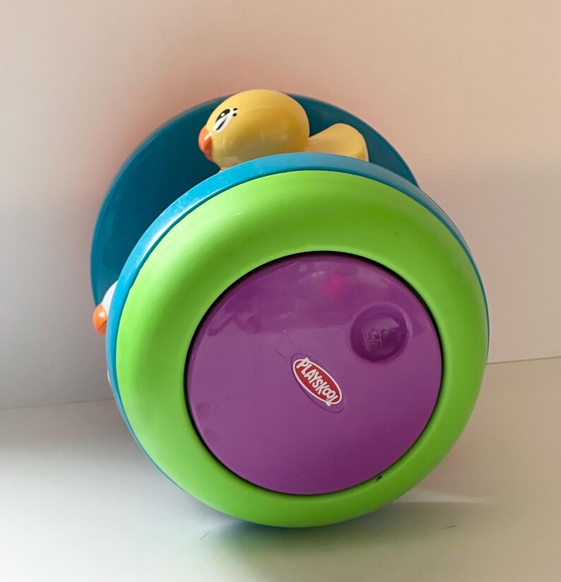 May include: A Playskool toy with a yellow duck on top. The toy is a combination of bright colors, including teal, green, and purple. The Playskool logo is visible on the purple surface. The toy is designed for young children.