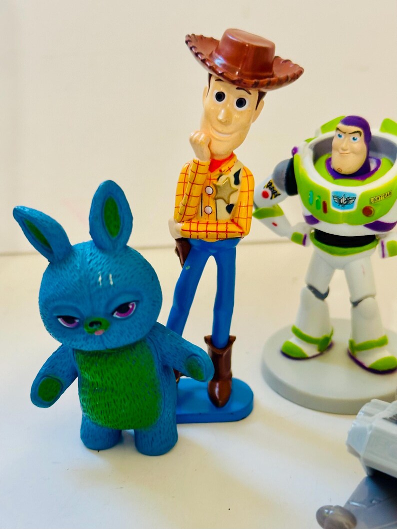 Peut inclure: Figurines de personnages de Toy Story, dont Woody avec un chapeau de cow-boy, Buzz l'&Eacute;clair dans une combinaison spatiale verte et blanche, et un personnage bleu en forme de lapin. Les figurines sont color&eacute;es.
