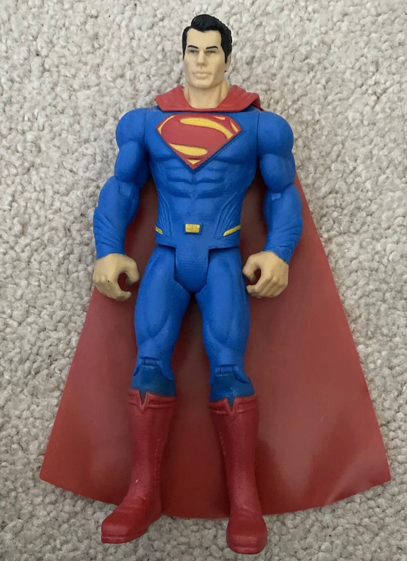May include: Superman action figure in a classic blue suit with a red cape and boots. The figure has a yellow and red Superman logo on the chest. The figure is approximately 6 inches tall.