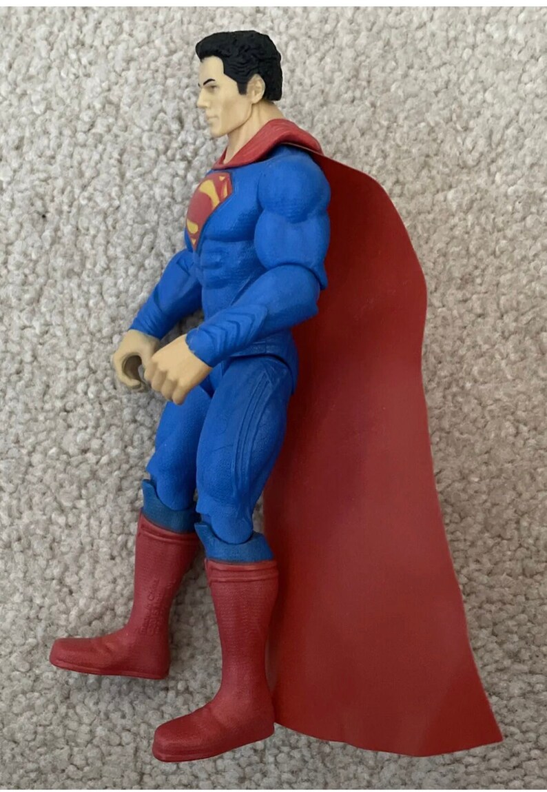 May include: A Superman action figure in a classic blue suit with a red cape and boots. The figure has a detailed face and the iconic Superman logo on the chest. The figure is posed in a dynamic stance.