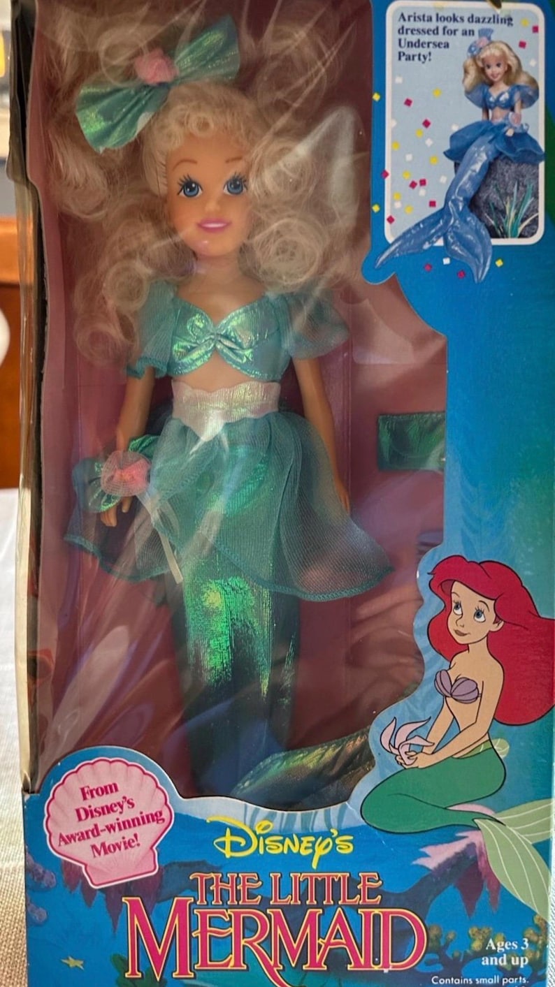 May include: A Disney's The Little Mermaid doll of Arista in a box. The doll is wearing a teal dress with a matching bow. The box features images of Ariel and the text "From Disney's Award-winning Movie!"