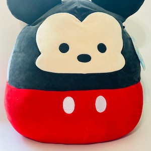 Op de afbeelding: Een pluche Mickey Mouse-kussen. Het kussen heeft een zwarte kop en oren, een cr&egrave;mekleurig gezicht en een rode body met twee witte knoopdetails. Het kussen is zacht en rond.
