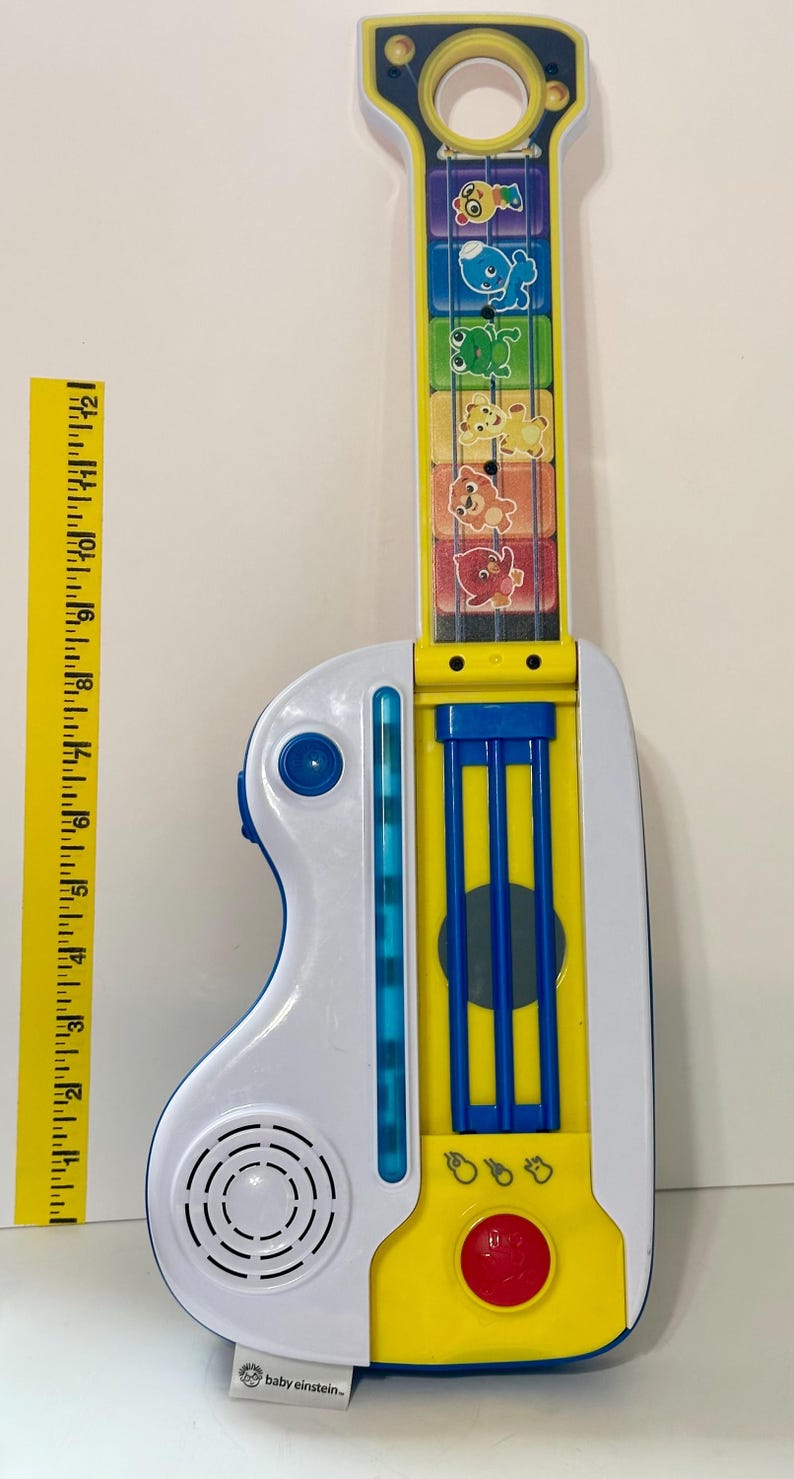 Pode incluir: Uma guitarra de brinquedo colorida com corpo branco e amarelo, detalhes azuis e um bot&atilde;o vermelho. A escala apresenta ilustra&ccedil;&otilde;es de animais. Uma r&eacute;gua amarela est&aacute; ao lado da guitarra. O brinquedo est&aacute; rotulado "baby einstein-".