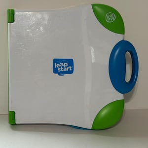 May include: White and blue LeapStart interactive learning system with a blue handle and green accents. The device has the LeapFrog logo and the words "leap start" printed on the front.