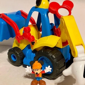 May include: A colorful toy construction vehicle with a Mickey Mouse figure. The vehicle is primarily blue, yellow, and red, with black tires. The Mickey Mouse figure is wearing an orange hard hat and work clothes. The toy is designed for children.