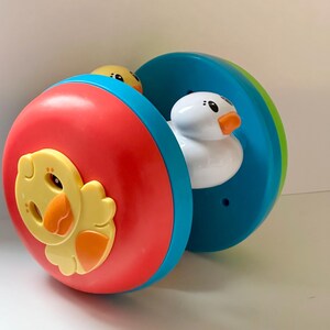 May include: A colorful toy featuring a red, blue, and green rolling wheel. The wheel has a yellow chick and a white duck inside. The toy is designed for children and has a playful appearance.