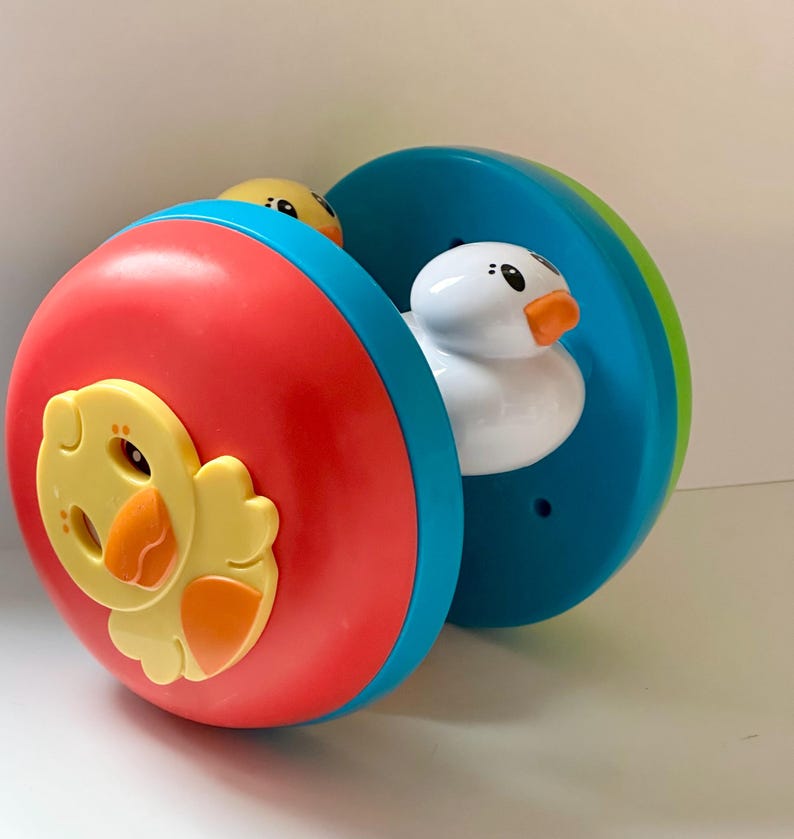 May include: A colorful toy featuring a red, blue, and green rolling wheel. The wheel has a yellow chick and a white duck inside. The toy is designed for children and has a playful appearance.