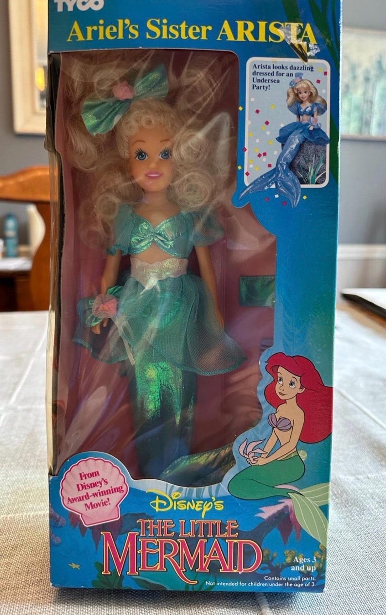 May include: A boxed doll of Ariel's sister Arista from Disney's The Little Mermaid. The doll has blonde hair and wears a teal outfit with a mermaid tail. The box features the movie's logo and the text "Ages 3 and up."