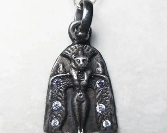 May include: Silver pendant necklace featuring a detailed depiction of a winged female figure with a horned head. The pendant is adorned with small clear and purple gemstones.