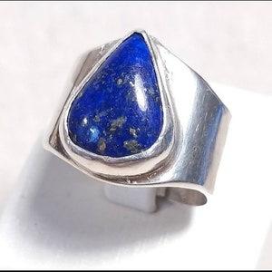 May include: A silver ring with a teardrop-shaped lapis lazuli stone set in a bezel setting. The ring has a wide band with a smooth, polished finish.