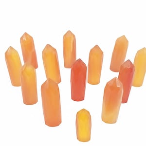 May include: A collection of orange and yellow crystal points arranged in a circular pattern. The crystals vary in shades from pale yellow to deep orange, with a faceted, polished appearance. The crystals are displayed against a white background.