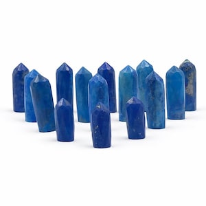 May include: A collection of blue crystal points in varying shades, arranged on a white background. The crystals have a faceted design and range in color from light to deep blue. The crystals are approximately 3 inches tall.