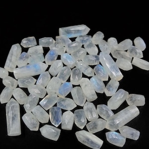 May include: A collection of polished moonstone crystals, each with a translucent, milky white appearance and subtle blue flashes. The crystals are various sizes and shapes, scattered against a black background, showcasing their natural beauty.